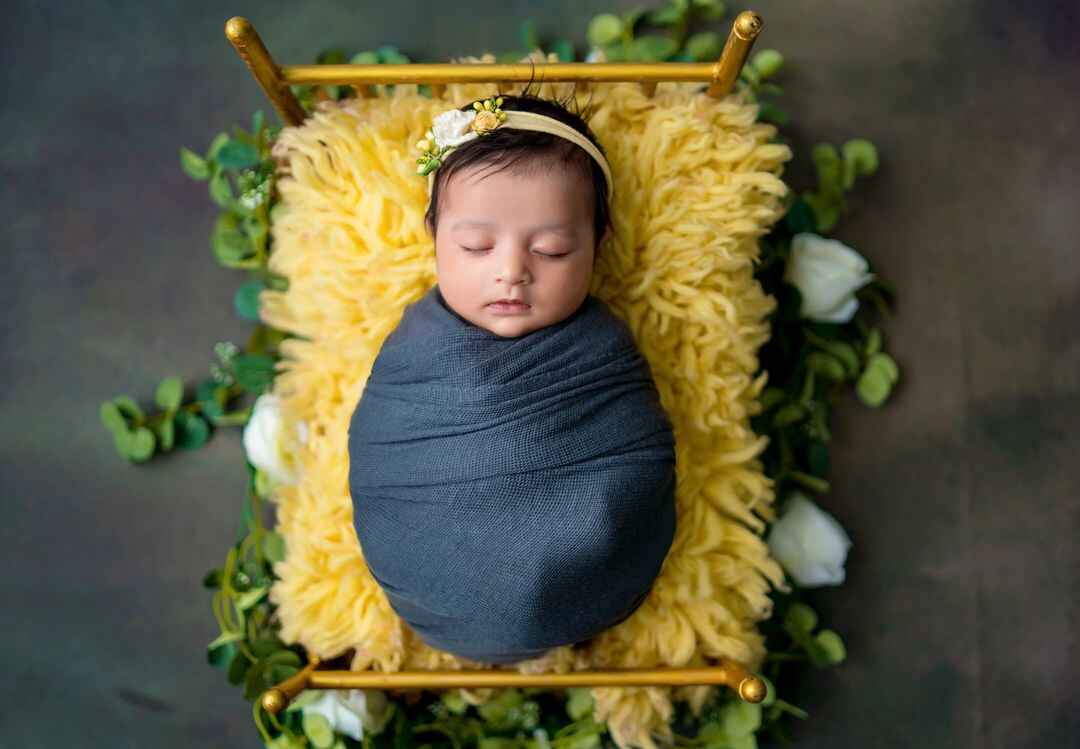 Endearing moment captured of a sleeping baby in a floral-mattress wooden bed, by professional baby photographers.
